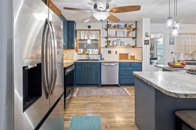 Kitchen featuring appliances with stainless steel finishes, blue cabinets, tasteful backsplash, light wood finished floors, and ceiling fan | Image 4