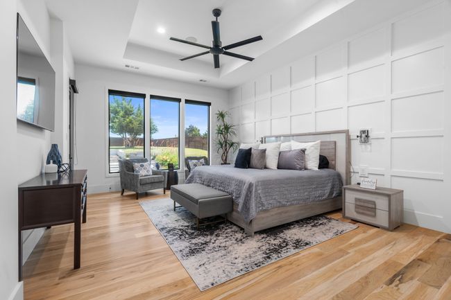 Bedroom featuring a tray ceiling, a decorative wall, light wood finished floors, and a ceiling fan | Image 13