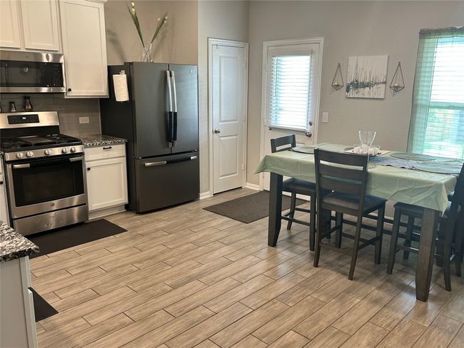Kitchen with appliances with stainless steel finishes, light wood-style flooring, tasteful backsplash, white cabinets, and dark stone counters | Image 11