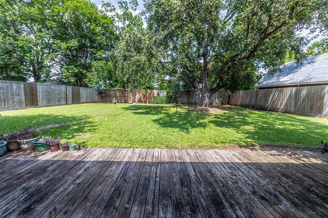 Spacious backyard with a wooden deck, lush green lawn, and mature trees, enclosed by a wooden fence—ideal for outdoor activities and relaxation. | Image 27