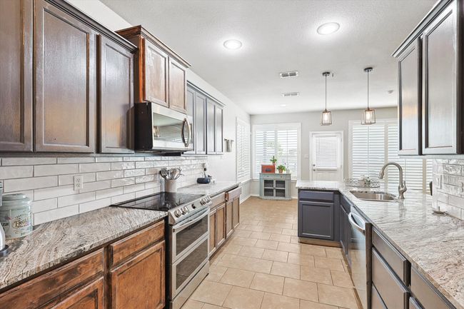 Kitchen featuring stainless steel appliances, decorative backsplash, light stone countertops, light tile patterned floors, and recessed lighting | Image 12