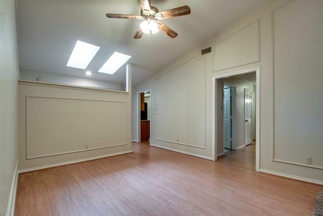 Empty room with a skylight, vaulted ceiling, wood finished floors, and ceiling fan | Image 6