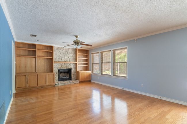 Unfurnished living room featuring a textured ceiling, ceiling fan, light wood-style flooring, baseboards, and a stone fireplace | Image 10
