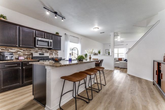 Kitchen with stainless steel appliances, a breakfast bar, decorative backsplash, dark stone countertops, and an island with sink | Image 11