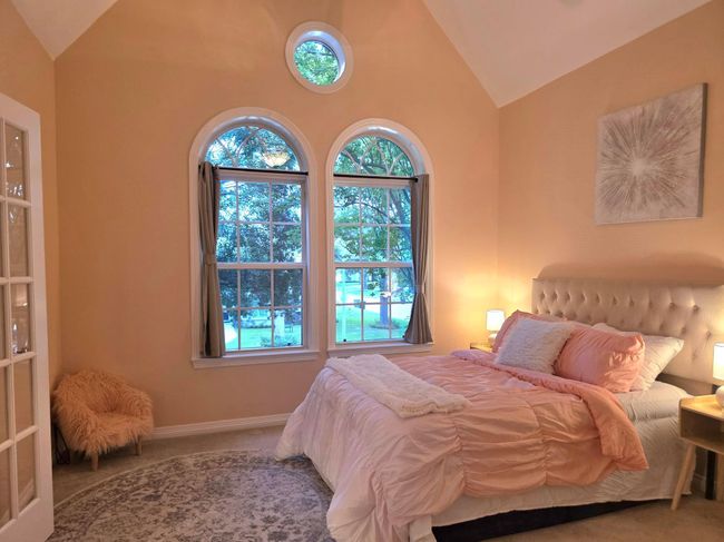 This cozy bedroom features high ceilings and large arched windows that allow plenty of natural light. It has soft peach walls creating a warm and inviting atmosphere. | Image 36