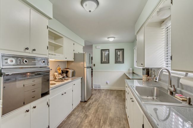 Kitchen featuring light wood finished floors, a wainscoted wall, oven, visible vents, and a sink | Image 6