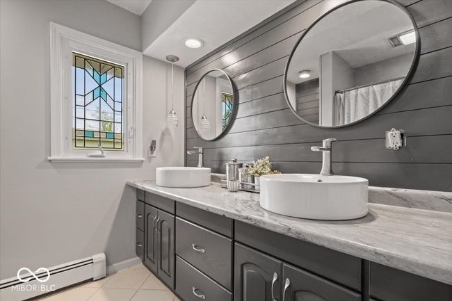 bathroom with a baseboard radiator, tile patterned flooring, baseboards, double vanity, and wood walls | Image 28