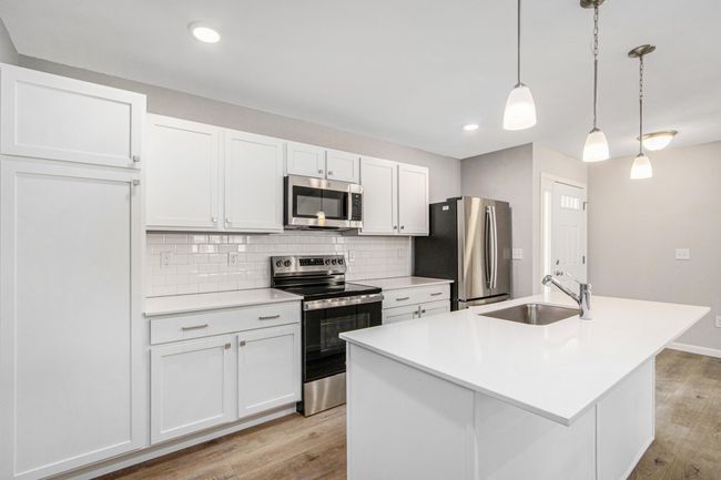 Bright, white kitchen cabinetry is accented by white quartz counters and tile backsplash. The kitchen island provides prep and sitting space and is accented by pendant lighting above. Stainless steel appliances are included! | Image 5