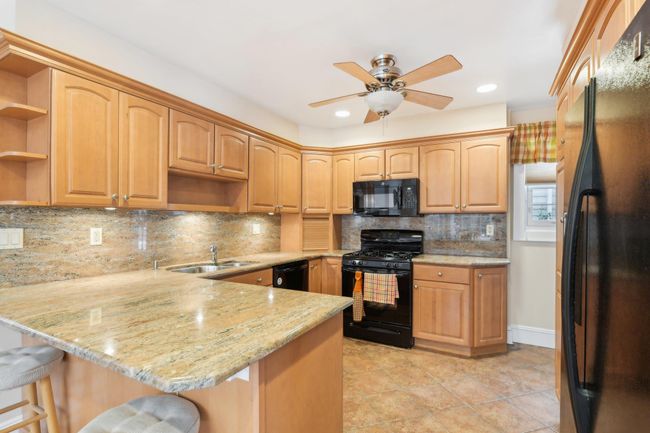 Kitchen featuring a breakfast bar, kitchen peninsula, sink, and black appliances | Image 7