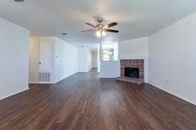 Unfurnished living room featuring dark wood-type flooring, ceiling fan, and a brick fireplace | Image 3