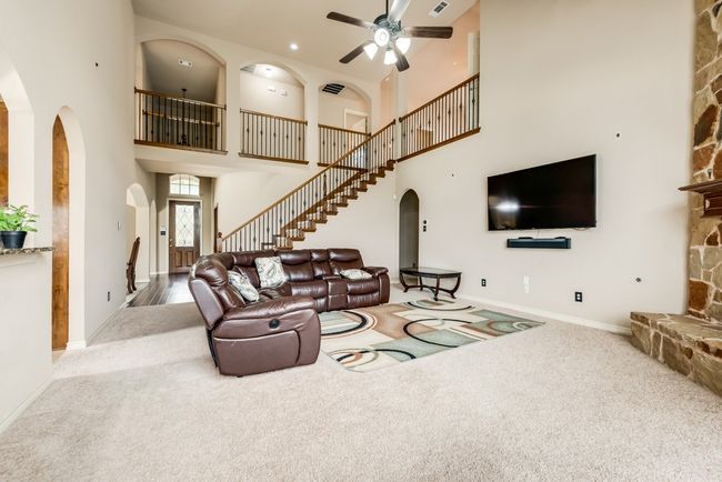 Carpeted living area with arched walkways, a high ceiling, a ceiling fan, baseboards, and stairs | Image 4