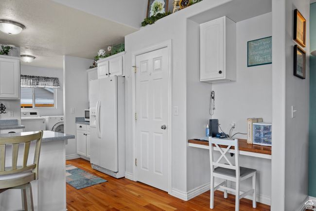 Kitchen featuring white cabinetry, light wood finished floors, washer and dryer, and white appliances | Image 11