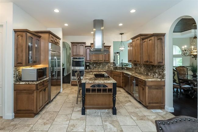 Kitchen with arched walkways, backsplash, island range hood, and stainless steel appliances | Image 18