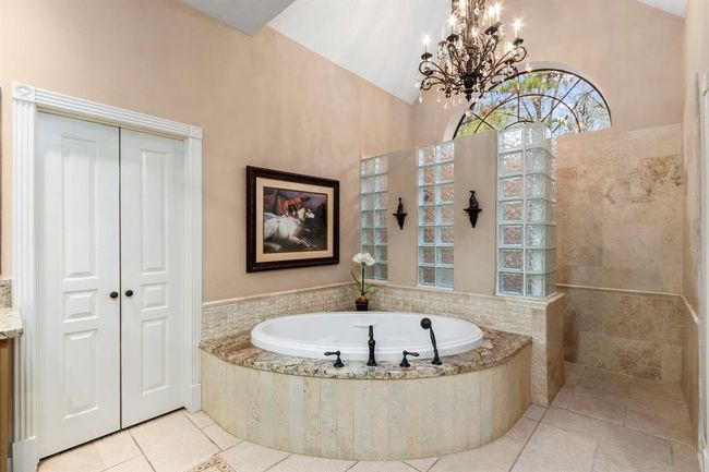 This deep, air jetted tub is surrounded by travertine basket weave accent tile and granite tub deck. A tub-filling faucet combined with a hand shower makes it both relaxing and convenient to bathe or clean. A gleaming chandelier above provides accent lighting for a relaxing bubble bath. The open and bright walk-in shower is nestled under the arched window with no shower door to clean. | Image 20