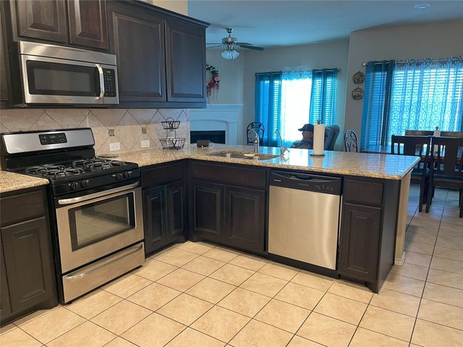 Kitchen featuring sink, light tile patterned floors, appliances with stainless steel finishes, kitchen peninsula, and backsplash | Image 7