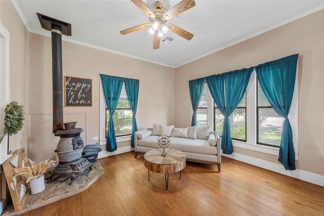 Living area featuring a wood stove, hardwood / wood-style flooring, a ceiling fan, and crown molding | Image 7