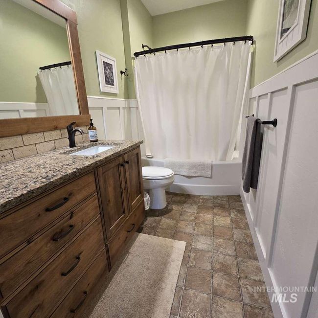 Full bath with stone finish flooring, vanity, shower / bathtub combination with curtain, and a wainscoted wall | Image 12