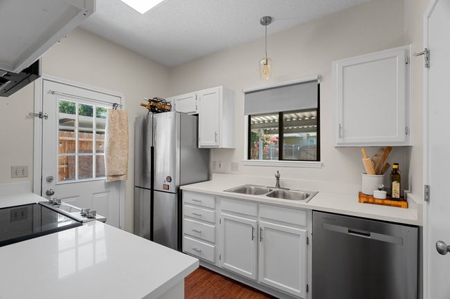 Kitchen with appliances with stainless steel finishes, white cabinetry, dark wood-style flooring, hanging light fixtures, and light countertops | Image 9
