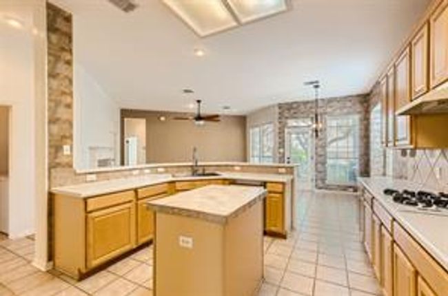 Kitchen featuring gas stovetop, light countertops, light tile patterned flooring, a kitchen island, and a peninsula | Image 6