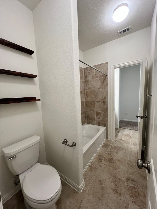 Full bath with a textured ceiling, bathing tub / shower combination, and light tile patterned floors | Image 24