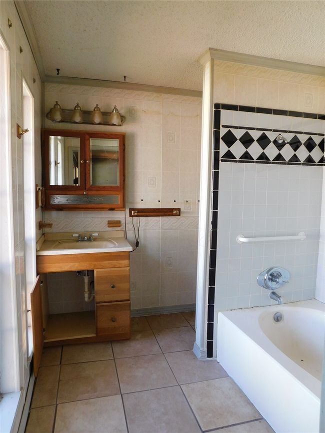 Bathroom featuring a textured ceiling, vanity, shower / bathing tub combination, tile walls, and tile patterned flooring | Image 17