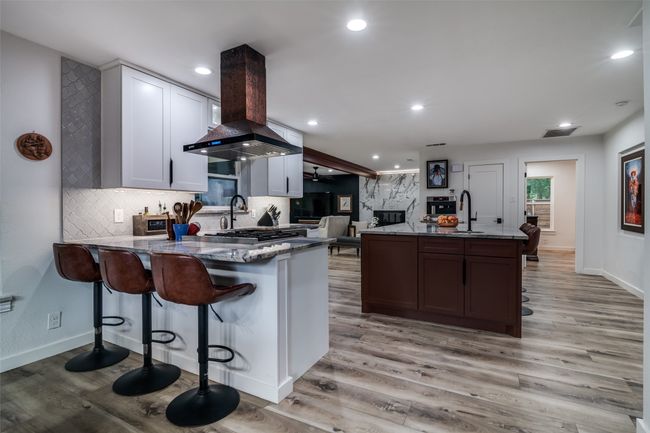 Kitchen with wall chimney exhaust hood, dark stone countertops, a premium fireplace, light wood finished floors, and recessed lighting | Image 15