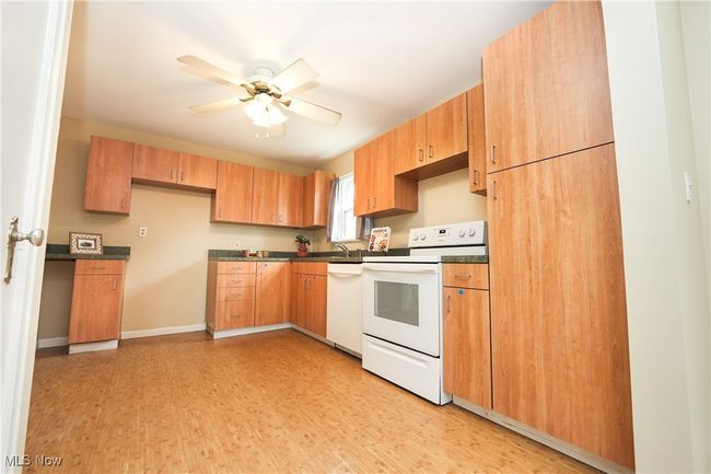 Kitchen with dark countertops, light wood-style floors, a ceiling fan, and white appliances | Image 13