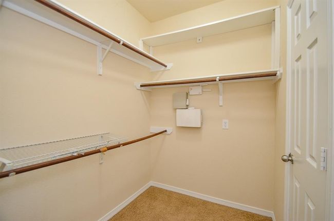 This photo shows a spacious walk-in closet with carpeted flooring, and multiple shelves and rods for ample storage. | Image 22