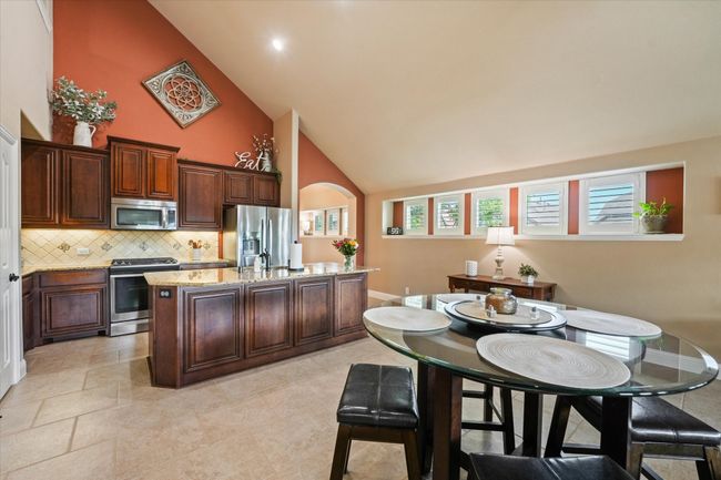 Kitchen featuring an island with sink, light stone counters, backsplash, appliances with stainless steel finishes, and high vaulted ceiling | Image 14