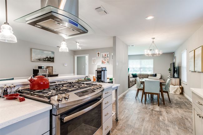 Kitchen featuring stainless steel range with gas cooktop, extractor fan, open floor plan, a chandelier, and hanging light fixtures | Image 13