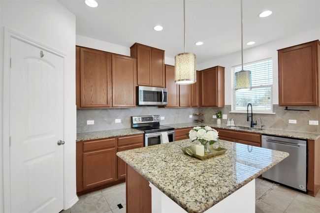Kitchen featuring a sink, hanging light fixtures, appliances with stainless steel finishes, light stone countertops, and tasteful backsplash | Image 14
