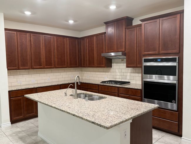 Kitchen featuring a sink, stainless steel appliances, under cabinet range hood, light stone counters, and a center island with sink | Image 9