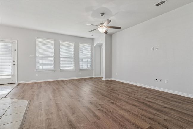 Unfurnished living room featuring a wealth of natural light, visible vents, wood finished floors, arched walkways, and ceiling fan | Image 8