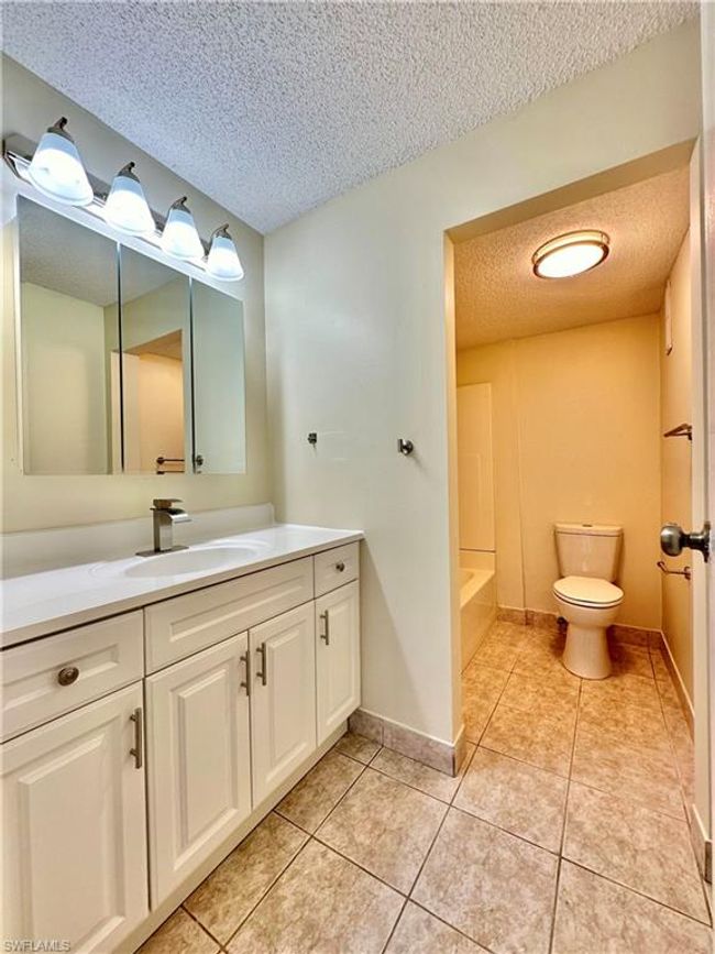 Bathroom featuring a textured ceiling, vanity, a tub to relax in, and tile patterned flooring | Image 8