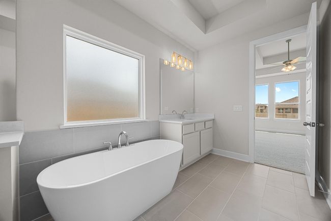 Bathroom with a raised ceiling, vanity, a ceiling fan, a freestanding tub, and tile patterned floors | Image 17