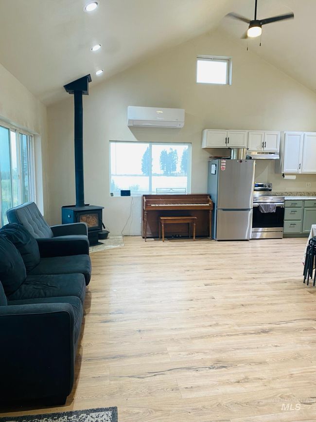 Living room featuring a wood stove, a wall mounted air conditioner, light wood-style flooring, high vaulted ceiling, and ceiling fan | Image 15