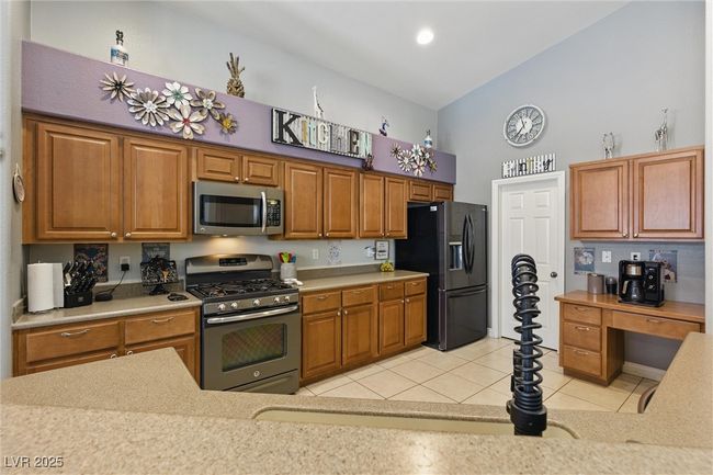 Kitchen with light countertops, brown cabinets, appliances with stainless steel finishes, and light tile patterned flooring | Image 9