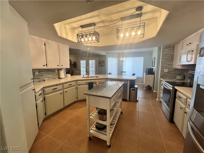 Kitchen with appliances with stainless steel finishes, a peninsula, a tray ceiling, decorative backsplash, and tile patterned floors | Image 17