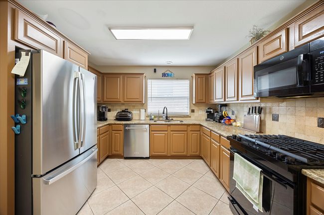 Kitchen with black appliances, a sink, tasteful backsplash, light tile patterned floors, and light stone counters | Image 12