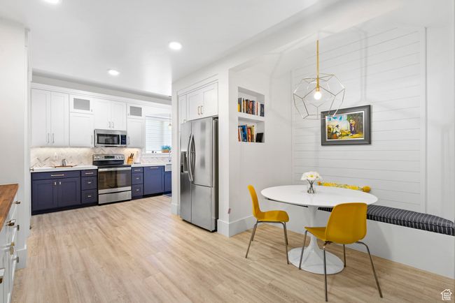 Kitchen featuring light wood-style flooring, blue cabinetry, white cabinets, appliances with stainless steel finishes, and decorative backsplash | Image 70