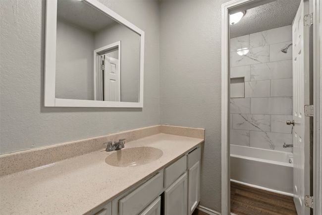 Bathroom with vanity, washtub / shower combination, a textured wall, a textured ceiling, and wood finished floors | Image 14
