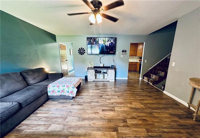 Living area with ceiling fan, wood finished floors, stairway, a textured ceiling, and baseboards | Image 6