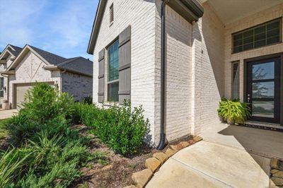 This is a modern home featuring a clean, white brick exterior with large windows, a covered entryway, and well-maintained landscaping, providing a welcoming curb appeal. | Image 3