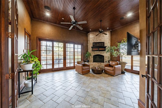 Living room with ceiling fan, a stone fireplace, wood ceiling, and french doors | Image 6