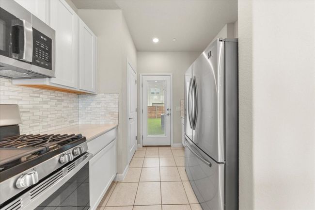 Kitchen featuring appliances with stainless steel finishes, decorative backsplash, white cabinetry, light countertops, and light tile patterned flooring | Image 13