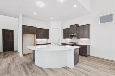 Kitchen featuring backsplash, sink, appliances with stainless steel finishes, light hardwood / wood-style flooring, and a center island with sink | Image 2