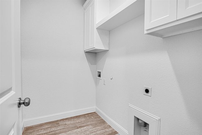 Laundry area featuring cabinet space, electric dryer hookup, light wood-type flooring, baseboards, and hookup for a gas dryer | Image 27