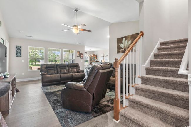 Living room with stairway, ceiling fan, wood finished floors, lofted ceiling, and a chandelier | Image 5