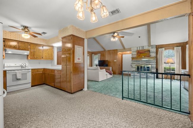 Kitchen with white electric range oven, under cabinet range hood, ceiling fan, light carpet, and wood walls | Image 15