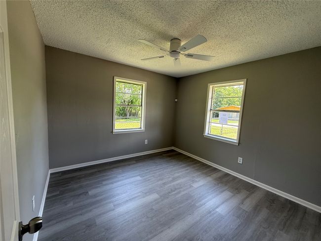 Empty room with ceiling fan, healthy amount of natural light, dark wood-type flooring, and a textured ceiling.View 1 | Image 8
